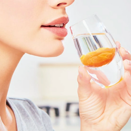 A person holding a glass with a Liposomal-VitaminC-Supplement yellow substance close to their mouth